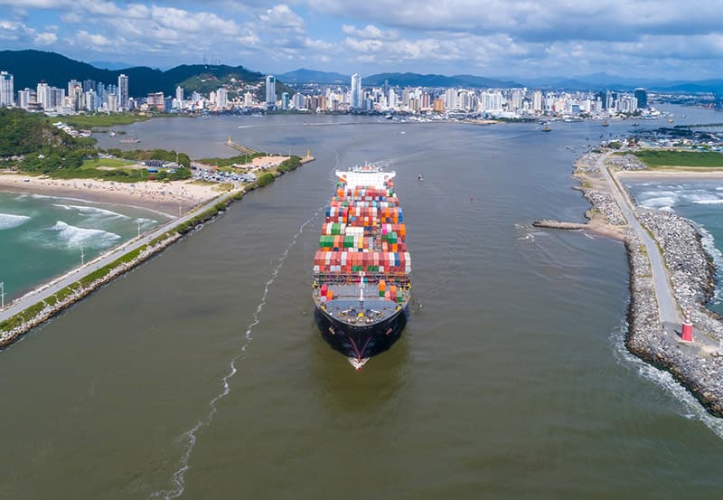 Navio porta-contêineres entrando no canal do rio Itajaí-Açu, com a cidade de Itajaí ao fundo